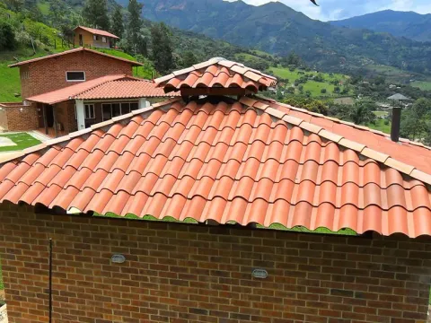 Casa campestre con teja de barro y montañas al fondo, obra cerca de Medellín